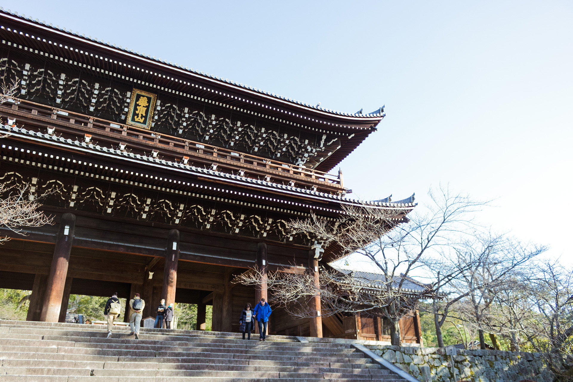 Roof of a buddhist temple, seen from below, six people walking below it on a staircase.